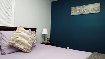 Un dormitorio con cama, almohadas, una mesita de noche con lámpara y una pared con un mapa y una cita motivacional.