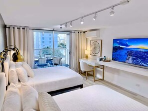 A modern hotel room with two beds, a desk, a chair, a TV, and a view of the city through large windows.