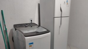 A compact kitchen with a washing machine, a refrigerator, and a broom leaning against the wall. - Suite Da Praia Ar-conditioned (Rio de Janeiro)