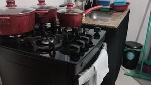 A kitchen with a stove, pots, a sink, and a window above the sink. - Suite Da Praia Ar-conditioned (Rio de Janeiro)