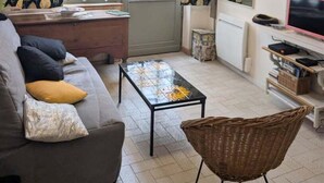 Een woonkamer met een bank, een salontafel, een rieten fauteuil, een televisie en behang met een patroon.