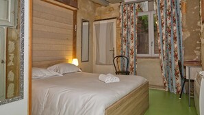 Een slaapkamer met een houten bed, een stoel, een bureau en een raam met bloemen gordijnen.