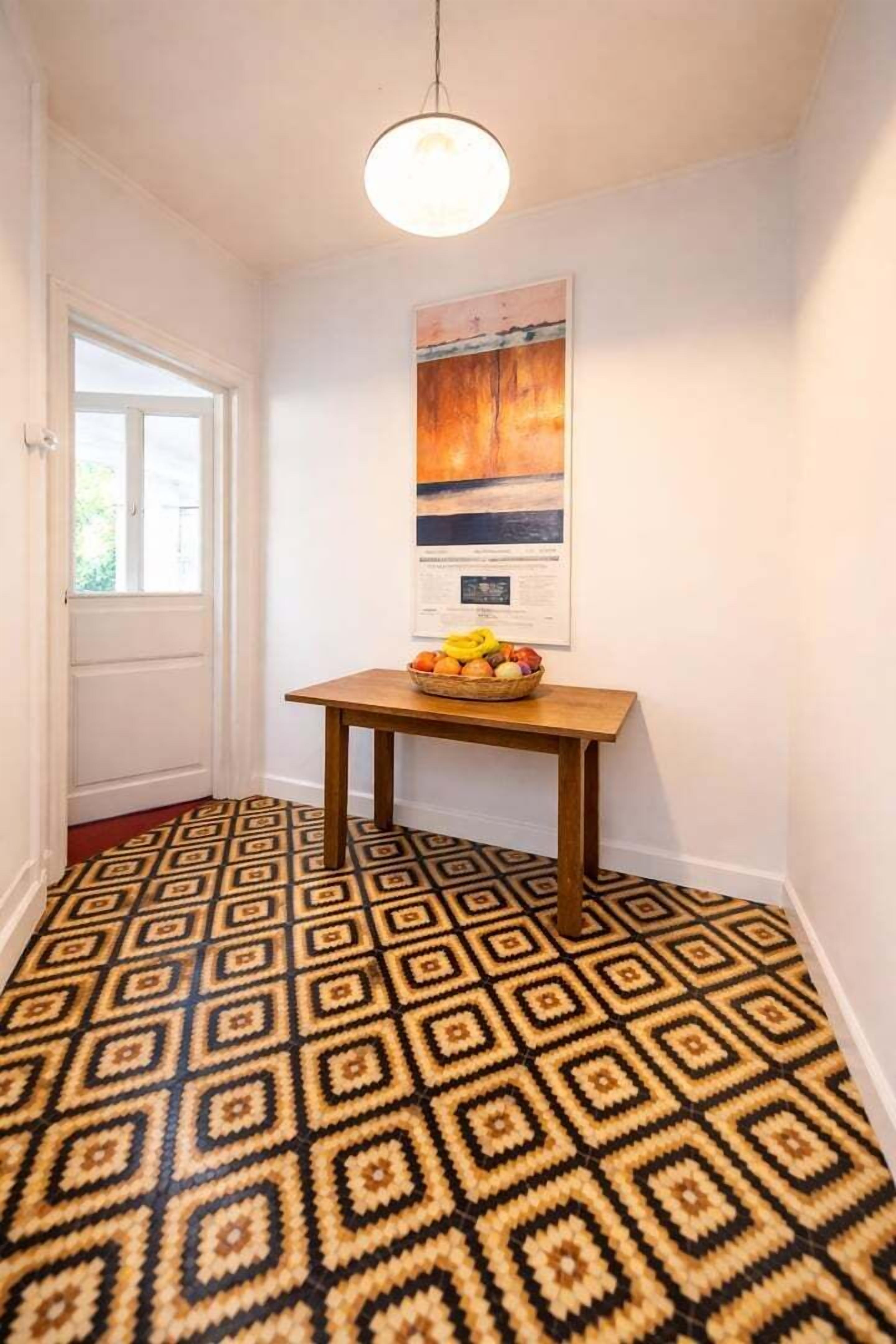 A hallway with patterned flooring, a wooden table with a fruit bowl, a hanging light fixture, and a door.