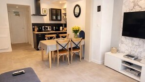 A modern living room with a TV, a dining area, and a kitchen in the background.