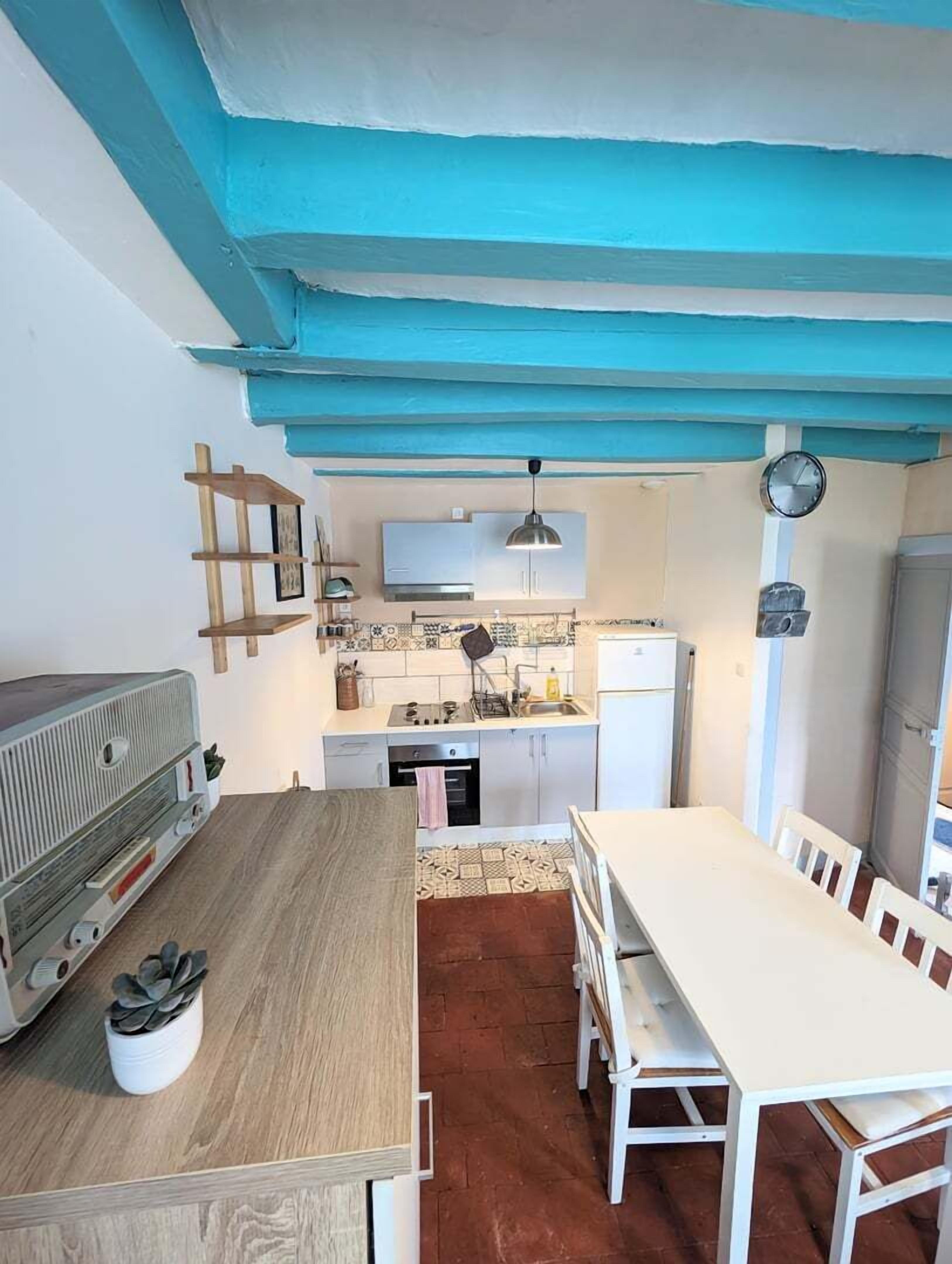 A compact kitchen with a white table, a wooden bench, and a vintage radio.