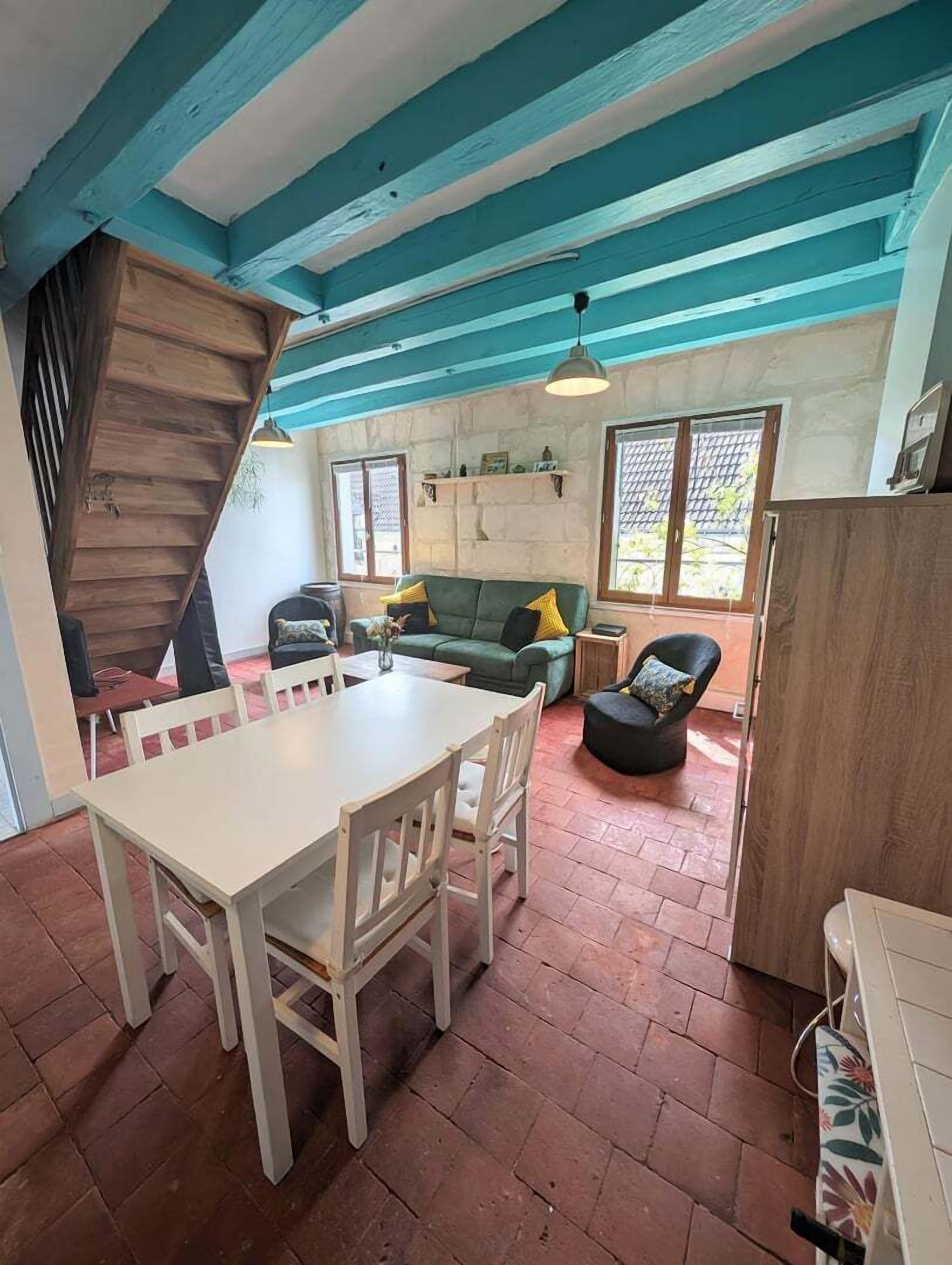 A cozy living area with a dining table and chairs, a green sofa, and a staircase.