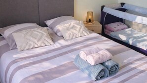 A neatly made bed with striped bedding, a bedside lamp, and a wall-mounted light fixture. - The source - Le Grand-Pressigny (Le Grand-Pressigny)