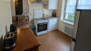 A compact kitchen with a gas stove, oven, white cabinets, a window with a view, and a hexagonal tiled floor. - The source - Le Grand-Pressigny (Le Grand-Pressigny)