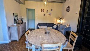 A dining area with a round wooden table and chairs, a sofa, and a wall-mounted clock. - The source - Le Grand-Pressigny (Le Grand-Pressigny)