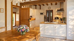 Eine Küche mit Holzbalken, weißen Schränken, einem Holztisch mit Stühlen und einem Blumenstrauß.