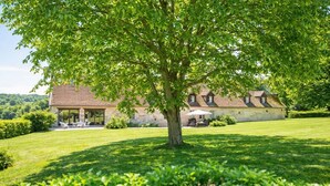 Ein Steinhäuschen mit großem Rasen, Gartenmöbeln und einem Baum im Vordergrund.