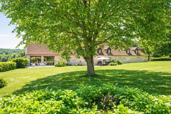Ein Steinhäuschen mit großem Rasen, Gartenmöbeln und einem Baum im Vordergrund.