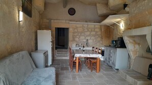 Una habitación acogedora con sofá, una mesa de comedor con sillas, una zona de cocina con fregadero y armarios, y una pared de piedra.