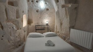 Un dormitorio con cama, almohadas, una mesita de noche con lámpara y un radiador.