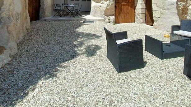 Un espacio al aire libre con paredes de piedra y suelo de grava, con mesas y sillas.