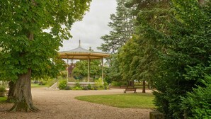 Un belvédère dans un parc, avec un chemin de gravier, des bancs et une végétation luxuriante.