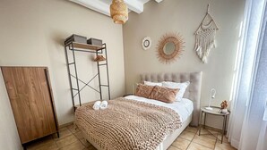 Une chambre à coucher comprenant un lit, une table de chevet, une lampe suspendue, un élément décoratif mural et une fenêtre avec des rideaux.