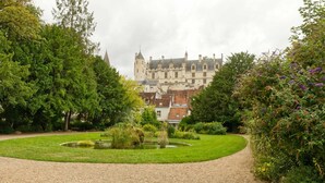 Un bâtiment historique à la façade symétrique, doté d’une cour centrale avec un bassin, et entouré d’une végétation luxuriante.