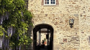 Ein Steinhaus mit einem zentralen Rundbogenportal, einem kleinen Fenster über der Tür und einer Glocke an der Wand.