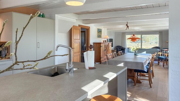 Una cocina moderna con una isla central, armarios de madera y un comedor con una mesa larga y sillas.