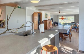 A modern kitchen with a central island, wooden cabinets, and a dining area with a long table and chairs.