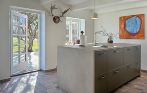 A modern kitchen with a central island, a large window, and a rustic deer head decoration.