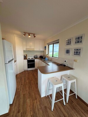 A compact kitchen with white cabinets, a wooden countertop, and two white stools. - Far Horizons 13 Trigg St Port Elliot Coastal Views (Port Elliot)