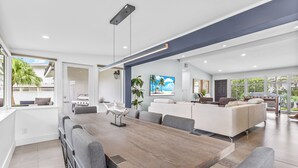 A modern living room with a large wooden dining table, grey sofas, and a view of the outdoors. - Waterfront Ft Lauderdale Retreat | Kayaks Included (Fort Lauderdale)