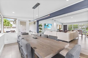 Ein modernes Wohnzimmer mit einem großen Holzesstisch, grauen Sofas und Blick ins Freie.