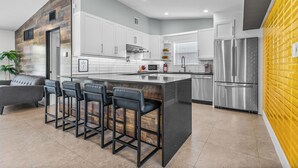 A modern kitchen with a central island, bar stools, stainless steel appliances, and a yellow accent wall. - Waterfront Ft Lauderdale Retreat | Kayaks Included (Fort Lauderdale)