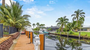 A wooden dock leading to a calm waterway with boats, surrounded by palm trees and a clear sky. - Waterfront Ft Lauderdale Retreat | Kayaks Included (Fort Lauderdale)
