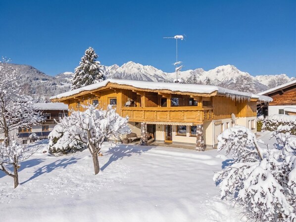 Un chalet en bois, dont le toit est recouvert de neige, entouré d’arbres et de montagnes également enneigés.