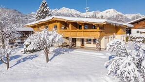 A wooden chalet with a snow-covered roof, surrounded by snow-covered trees and mountains in the background. - Alpine Holiday Apartment with Balcony (Söll)