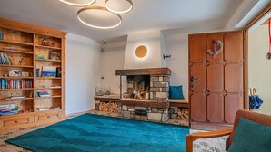 A cozy living room with a stone fireplace, a wooden bookshelf, and a teal rug. - Alpine Holiday Apartment with Balcony (Söll)