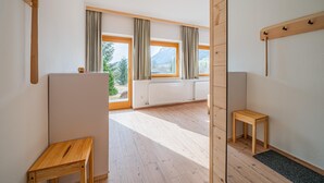 Une pièce spacieuse avec un plancher en bois, de grandes fenêtres avec des rideaux, un radiateur et une petite table en bois.