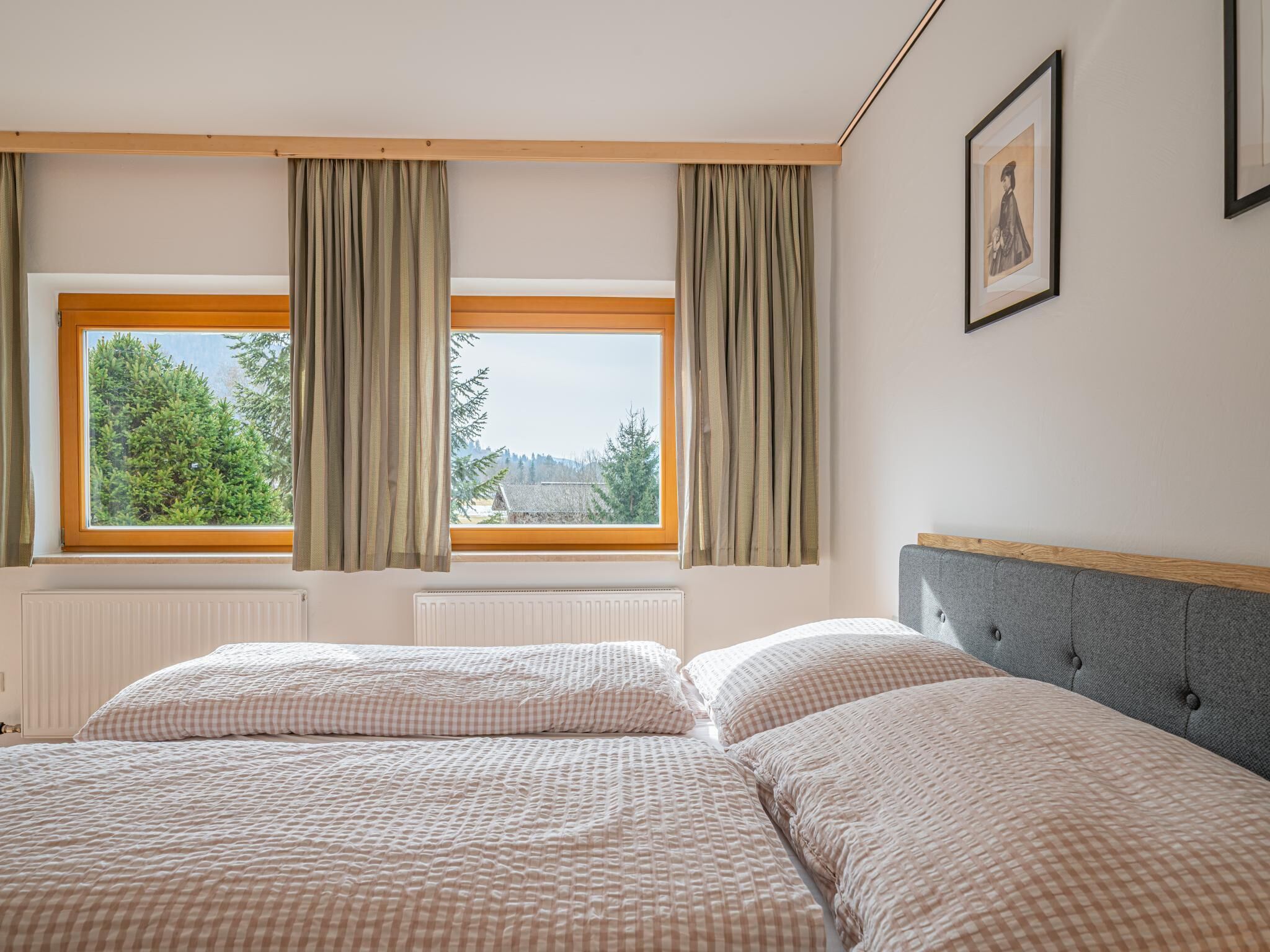 Une chambre avec deux lits, une fenêtre avec des rideaux, un radiateur et un tableau encadré au mur.