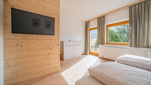 Une chambre avec des lambris en bois, un lit, une petite armoire blanche et une fenêtre avec des rideaux.