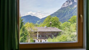 Un bâtiment rustique, doté d’un toit en pente, entouré d’une végétation luxuriante et avec des montagnes en arrière-plan.