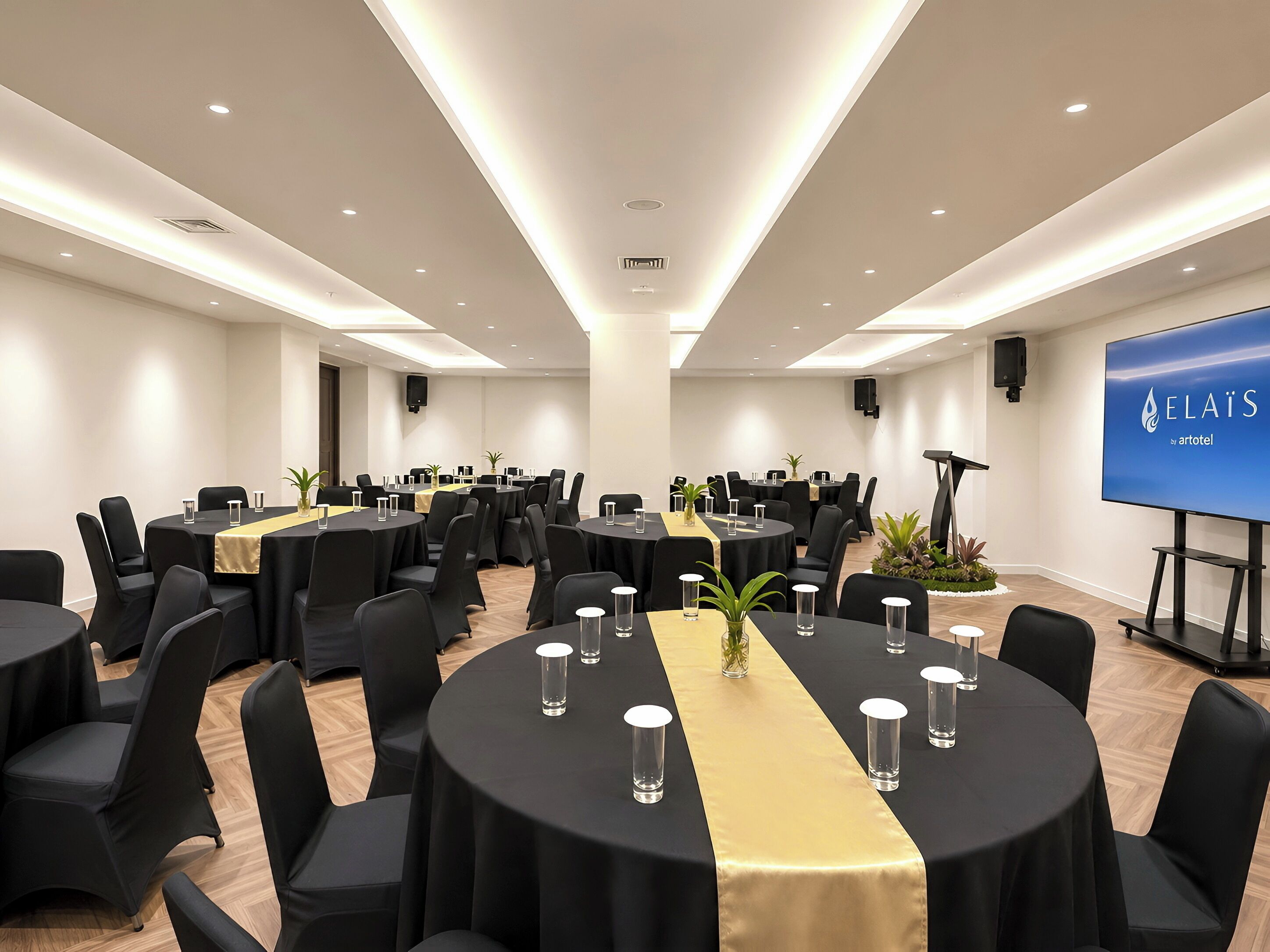 A conference room with round tables, black chairs, and a golden table runner.