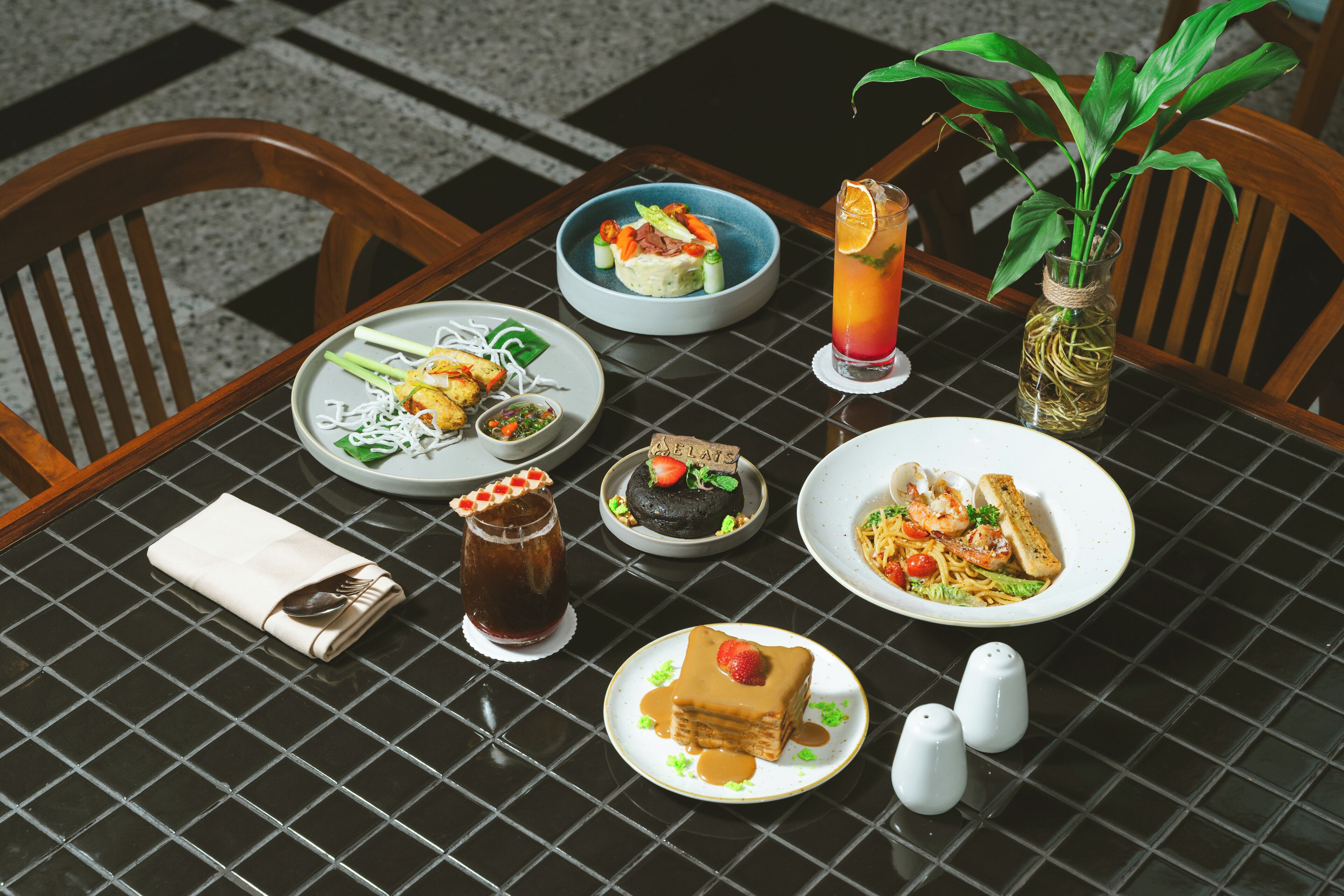 Une table dressée avec différents plats, une boisson et une plante.
