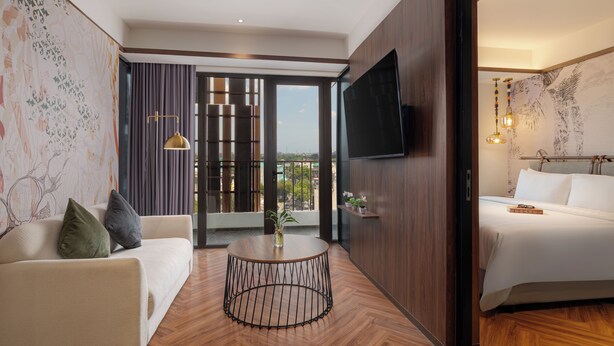 Ett hotellrum med en soffa, ett runt soffbord, en säng, en tv och utsikt genom en glasdörr.