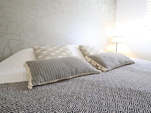Un lit avec une literie et des oreillers à motifs, un mur orné d’un motif floral et une lampe de chevet.