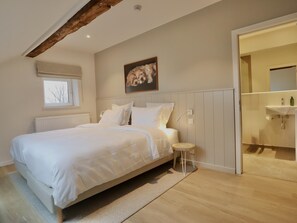 A bedroom with a large bed, a small stool, a window, and a bathroom visible through an open door.