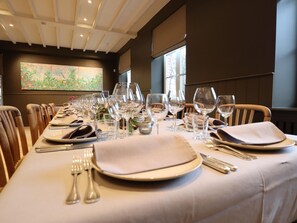 A dining table set with multiple wine glasses, plates, and cutlery, with a large abstract painting on the wall behind.