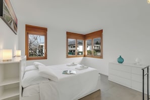 Une chambre à coucher moderne, avec un lit, des tables de chevet, une commode et de grandes fenêtres.
