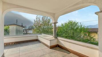Ein Balkon mit Fliesenboden, einer Steinsäule und Blick auf Häuser und Bäume.
