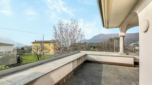 Una terraza en la azotea con vistas a un árbol, un edificio y montañas al fondo.
