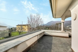 Eine Dachterrasse mit Blick auf einen Baum, ein Gebäude und Berge im Hintergrund.