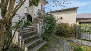 A stone staircase leading to a building with a balcony, surrounded by greenery and a clear sky. - Casa Di Bea - Lugano 1BR With Terrace & Parking (Lugano)