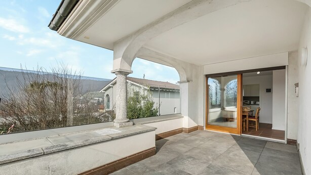 A balcony with stone flooring, a wooden table, and a chair, overlooking a residential area. - Casa Di Bea - Lugano 1BR With Terrace & Parking (Lugano)
